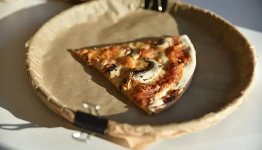 Kawałek pizzy 50 cm, z pieczarkami i serem, na papierowym talerzu. Zastanawiasz się nad jej kcal?