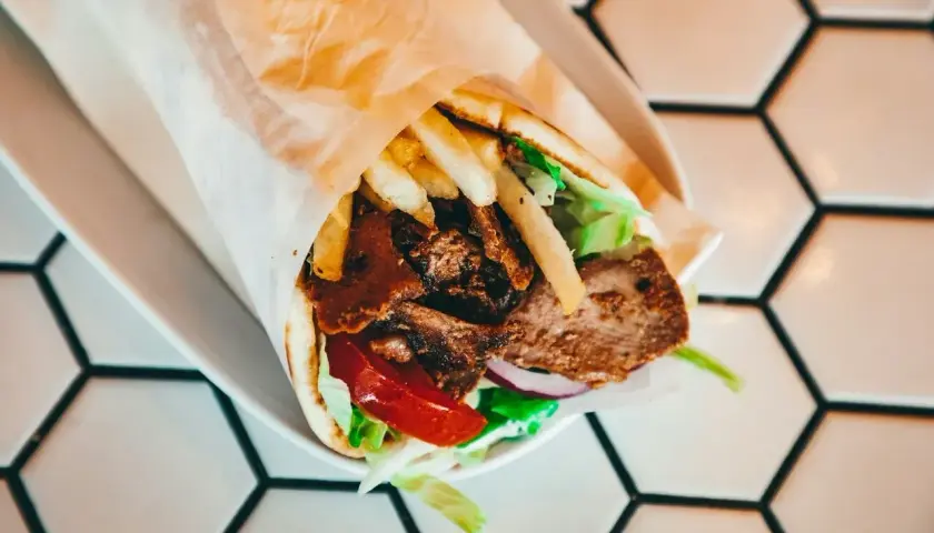 Pyszny gyros w placku tortilli z mięsem, frytkami i warzywami. Trudno określić, ile waży jeden placek tortilli, ale ten wygląda na sycący!