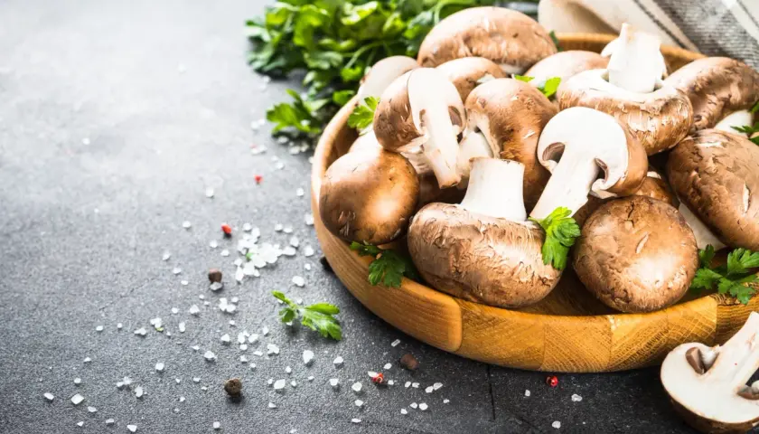 Pieczarki w drewnianej misce z natką pietruszki i solą na ciemnym tle.