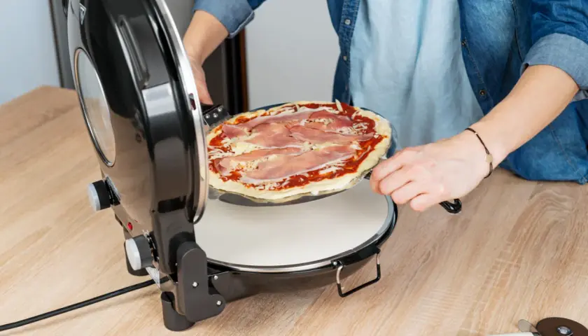 Osoba wkłada do piecyka okrągłą pizzę z szynką i serem, gotową do pieczenia. To będzie pyszna pizza Dziuzeppe!
