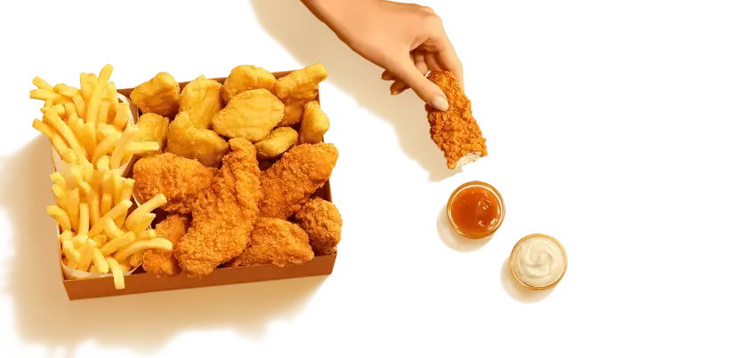 Pudełko McDonald's z kurczakiem i frytkami. Ręka zanurza kawałek kurczaka w sosie. Sprawdź kcal!