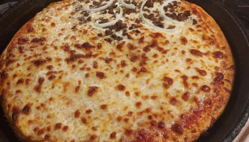 Pyszna pizza supreme z Pizza Hut, z mięsem mielonym i krążkami cebuli, zapieczona na złoto w żeliwnej patelni.