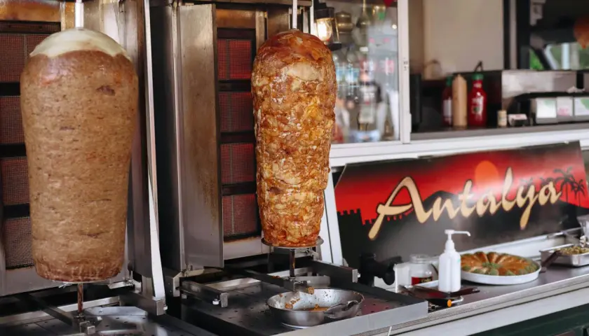 Dwa pionowe rożna z mięsem na kebab, obok znak "Antalya". Zastanawiasz się, ile kosztuje kebab?