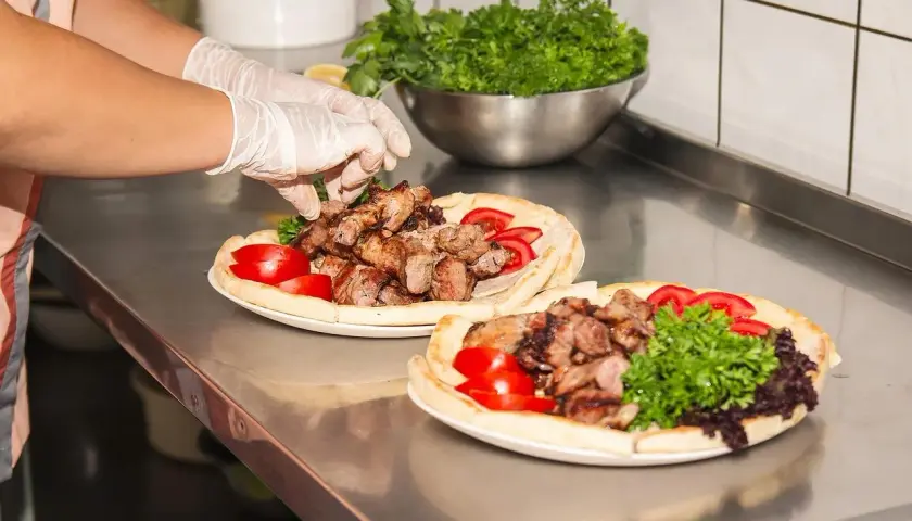 Ręce w rękawiczkach układają mięso na plackach z pomidorami i natką. Pyszny gemuse kebab gotowy do podania.