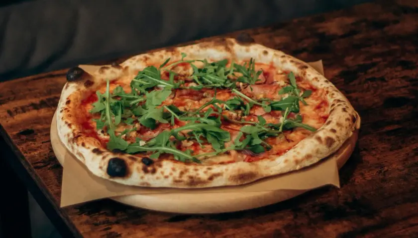 Pyszna pizza z rukolą i szynką, dzieło prawdziwego pizzaiolo, na drewnianym stole.