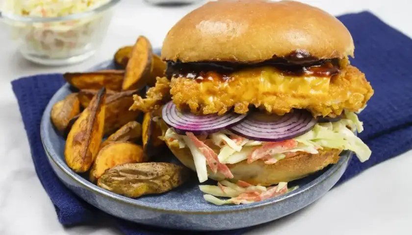 Drwal z kurczakiem w panierce, z serem, czerwoną cebulą i surówką coleslaw, podany z pieczonymi ziemniakami.