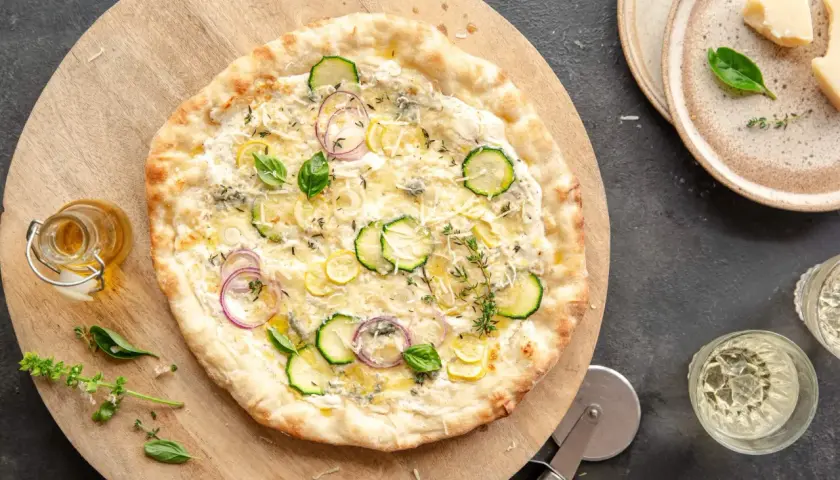 Pyszna pizza bianca z cukinią, cebulą i cytryną, ozdobiona bazylią i tymiankiem.