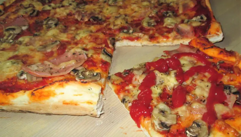 Pyszna pizza supreme z szynką i pieczarkami, polana ketchupem. Idealna na spotkanie z przyjaciółmi.
