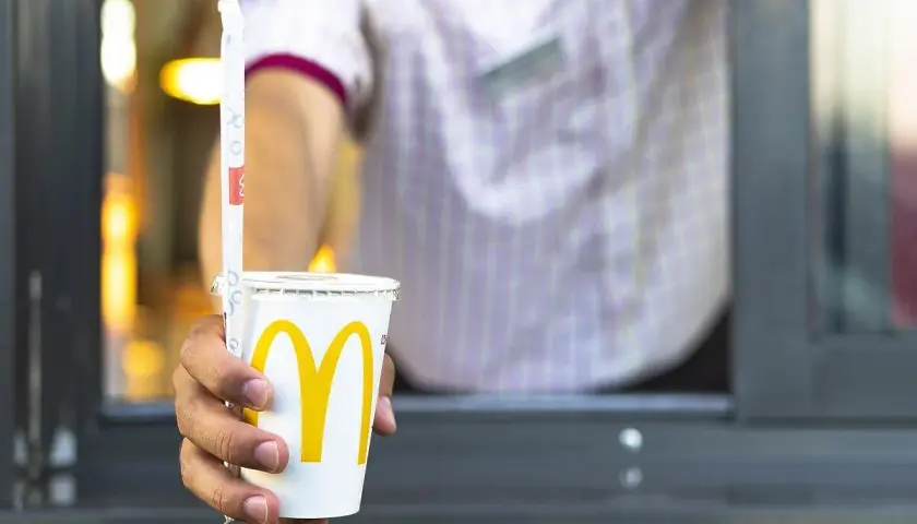 Dłoń podaje kubek z logo McDonald's, prawdopodobnie cappuccino. Warto sprawdzić cappuccino McDonald kcal przed zamówieniem.