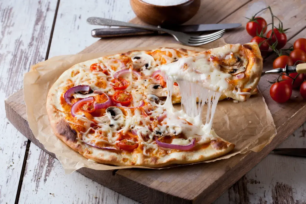 Rozciągający się ser z pizzy z pomidorami, cebulą i pieczarkami na desce.