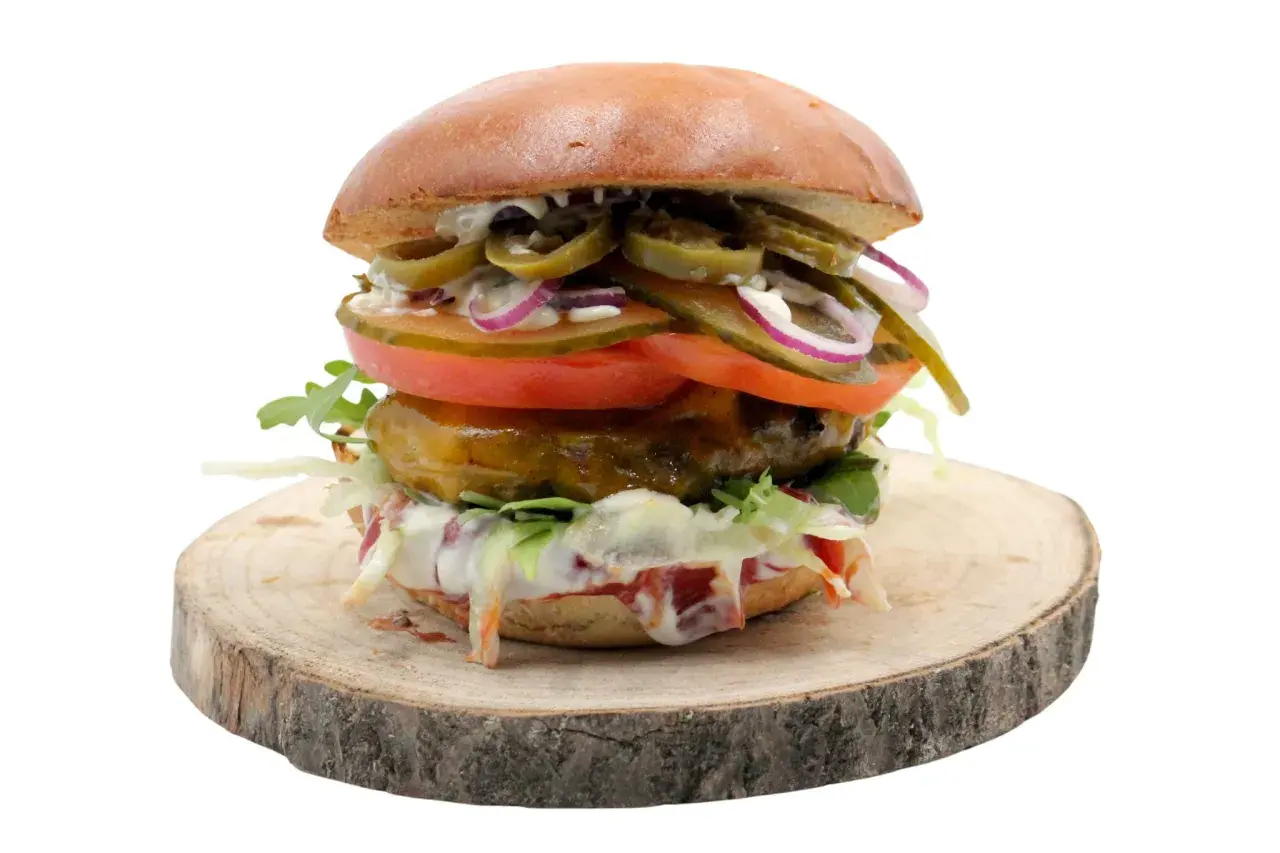 Burger z jalapeño, pomidorem, cebulą i sałatą na drewnianym krążku.