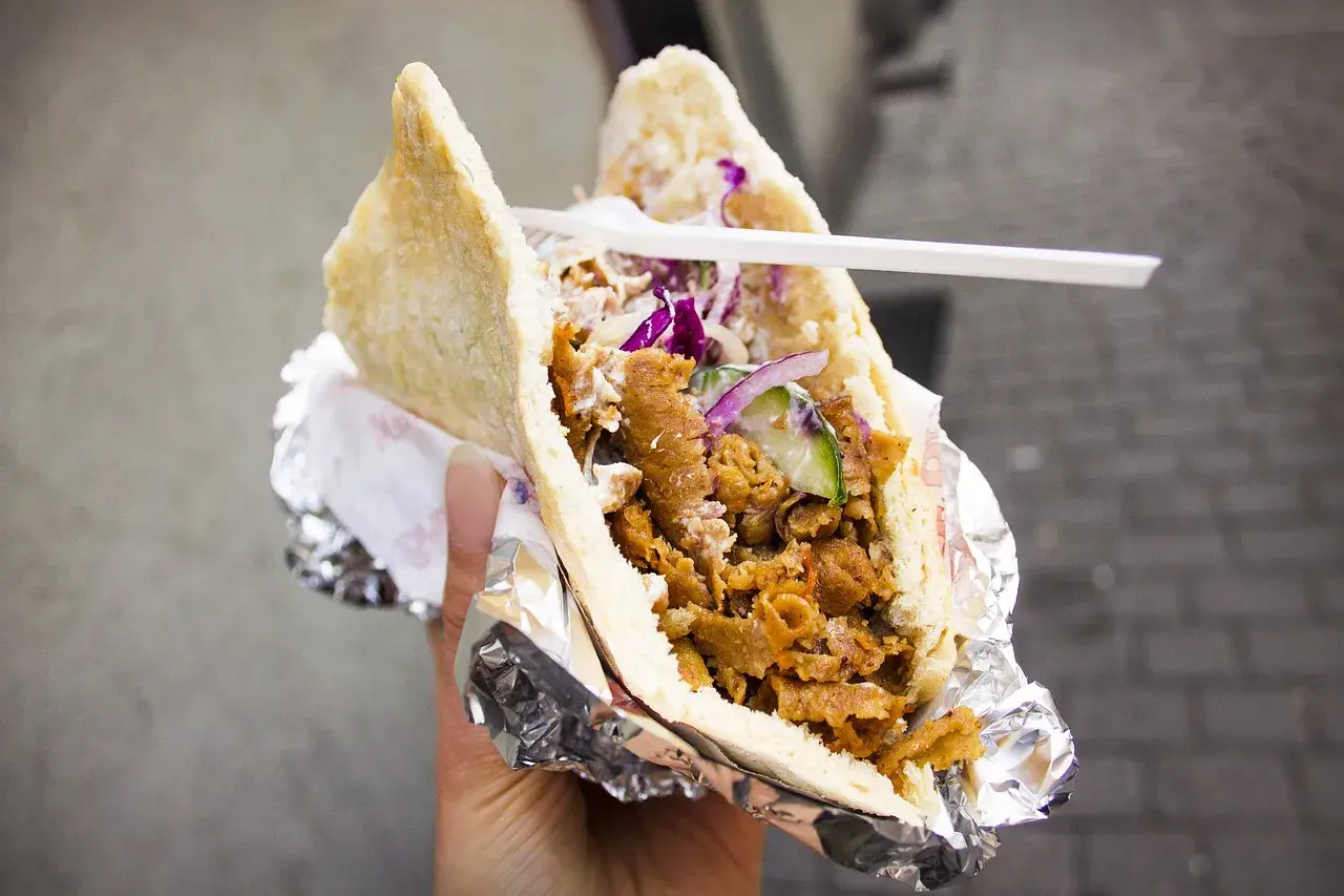 Pyszny kebab w bułce z mięsem, warzywami i sosem. To danie, które swoją popularność zawdzięcza podróżom i wymianie kulturowej, pokazując, skąd pochodzi kebab.