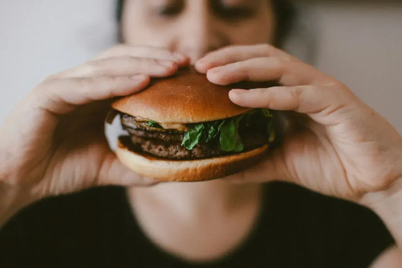 Ręce trzymają soczystego burgera, przypominającego mcroyal sklad. Mięso, sałata i bułka wyglądają apetycznie.
