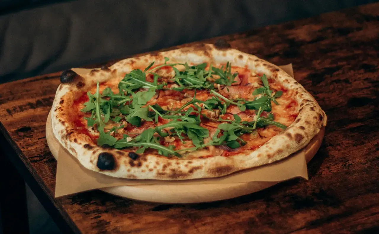 Pyszna pizza z rukolą i szynką, dzieło prawdziwego pizzaiolo, na drewnianym stole.