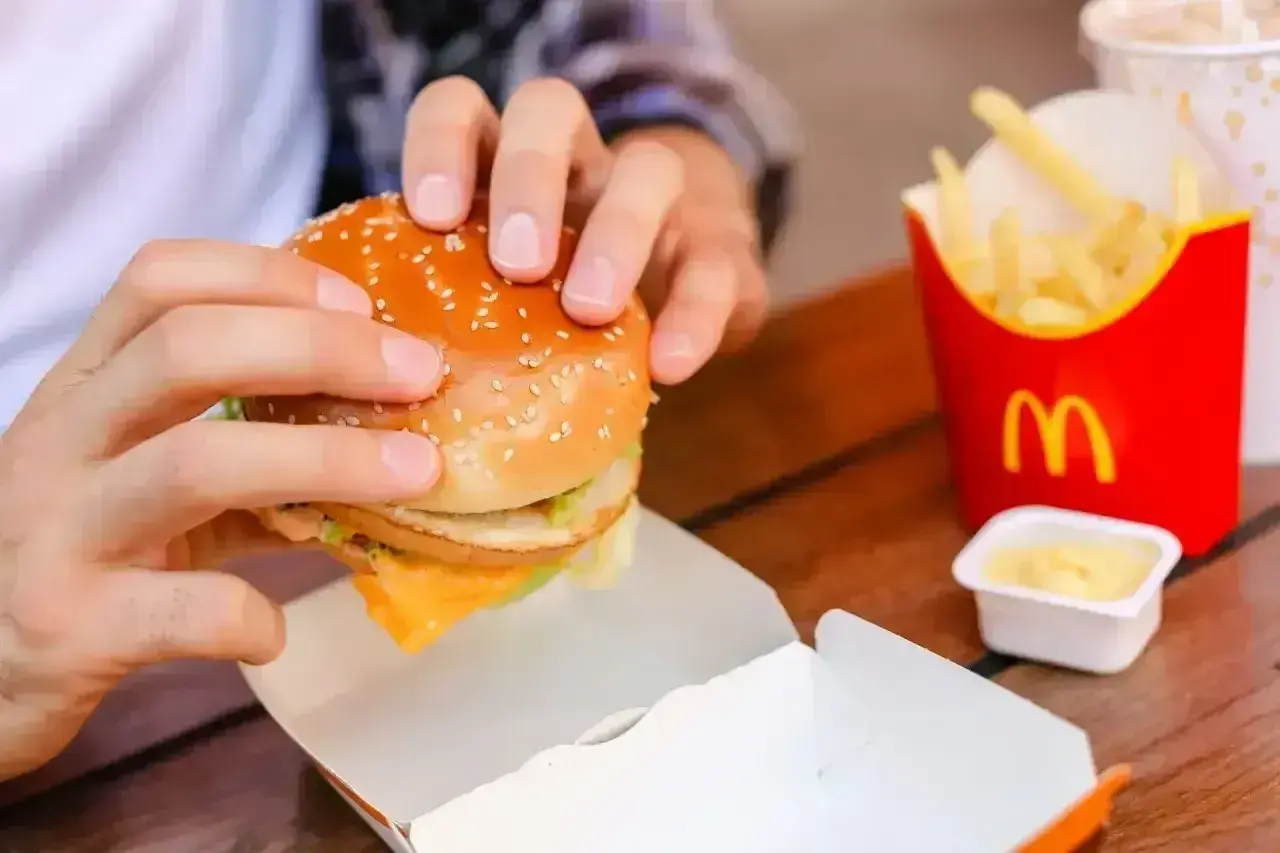 Ręce trzymają burgera z McDonald's, obok frytki i sos śmietanowy McDonald. Idealny zestaw na szybki posiłek.