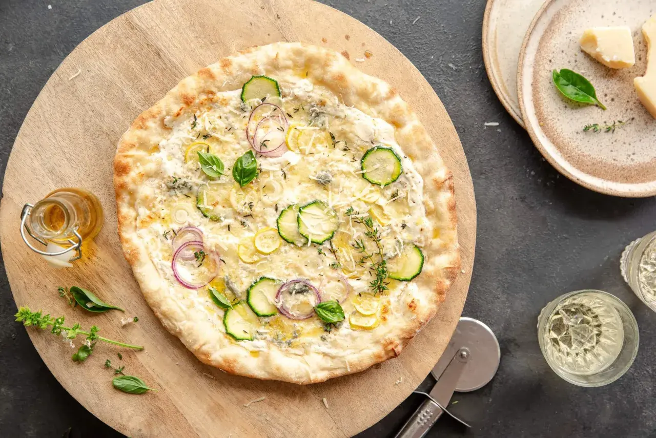 Pyszna pizza bianca z cukinią, cebulą i cytryną, ozdobiona bazylią i tymiankiem.