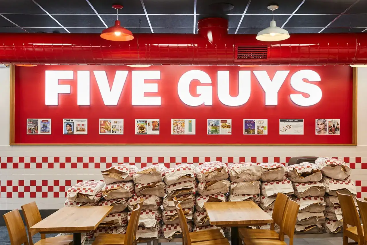 Wnętrze restauracji Five Guys Polska. Stosy papierowych toreb z logo marki piętrzą się przed ścianą z czerwonymi i białymi kwadratami.