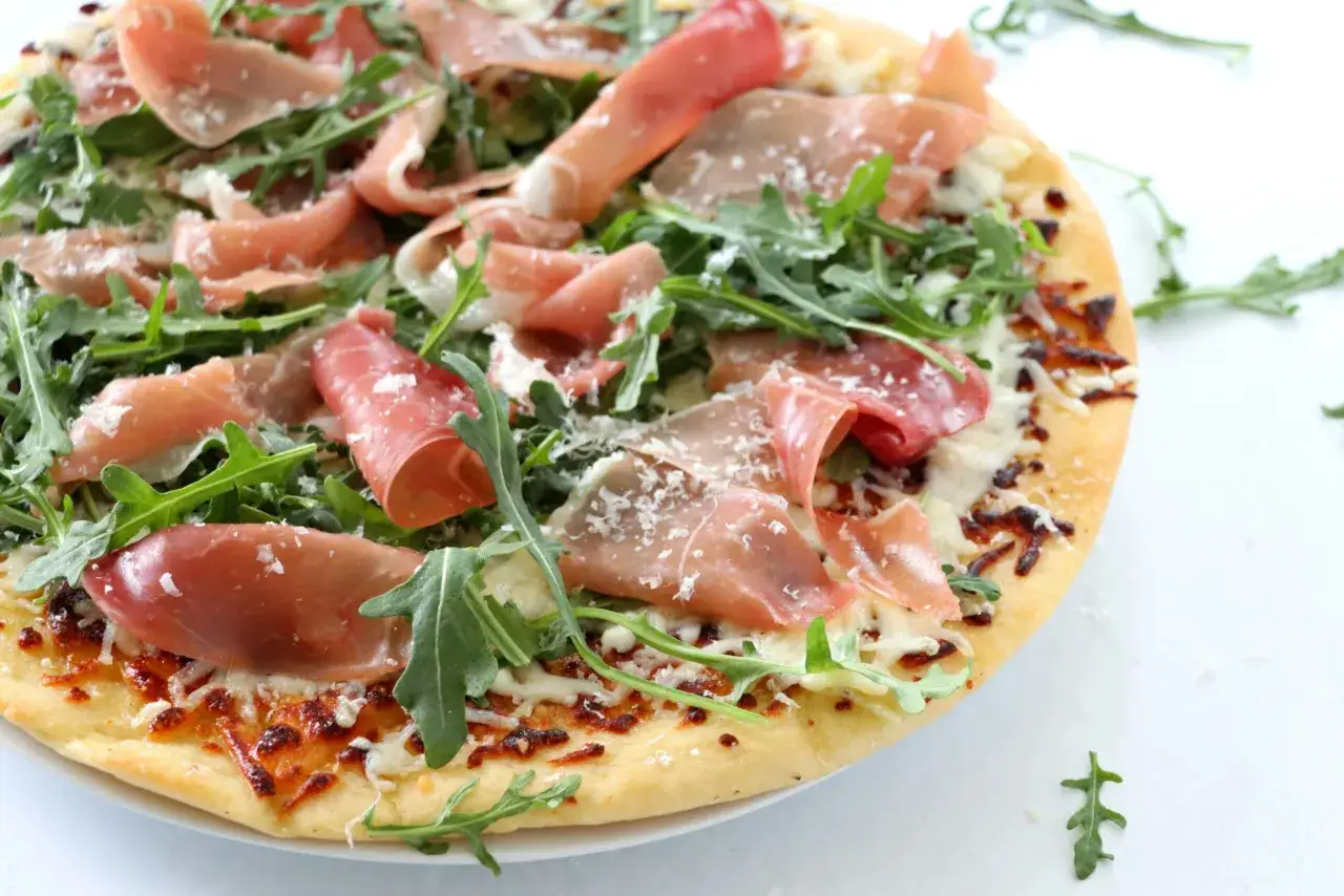 Pyszna pizza prosciutto z rukolą i parmezanem, idealna na szybki lunch.