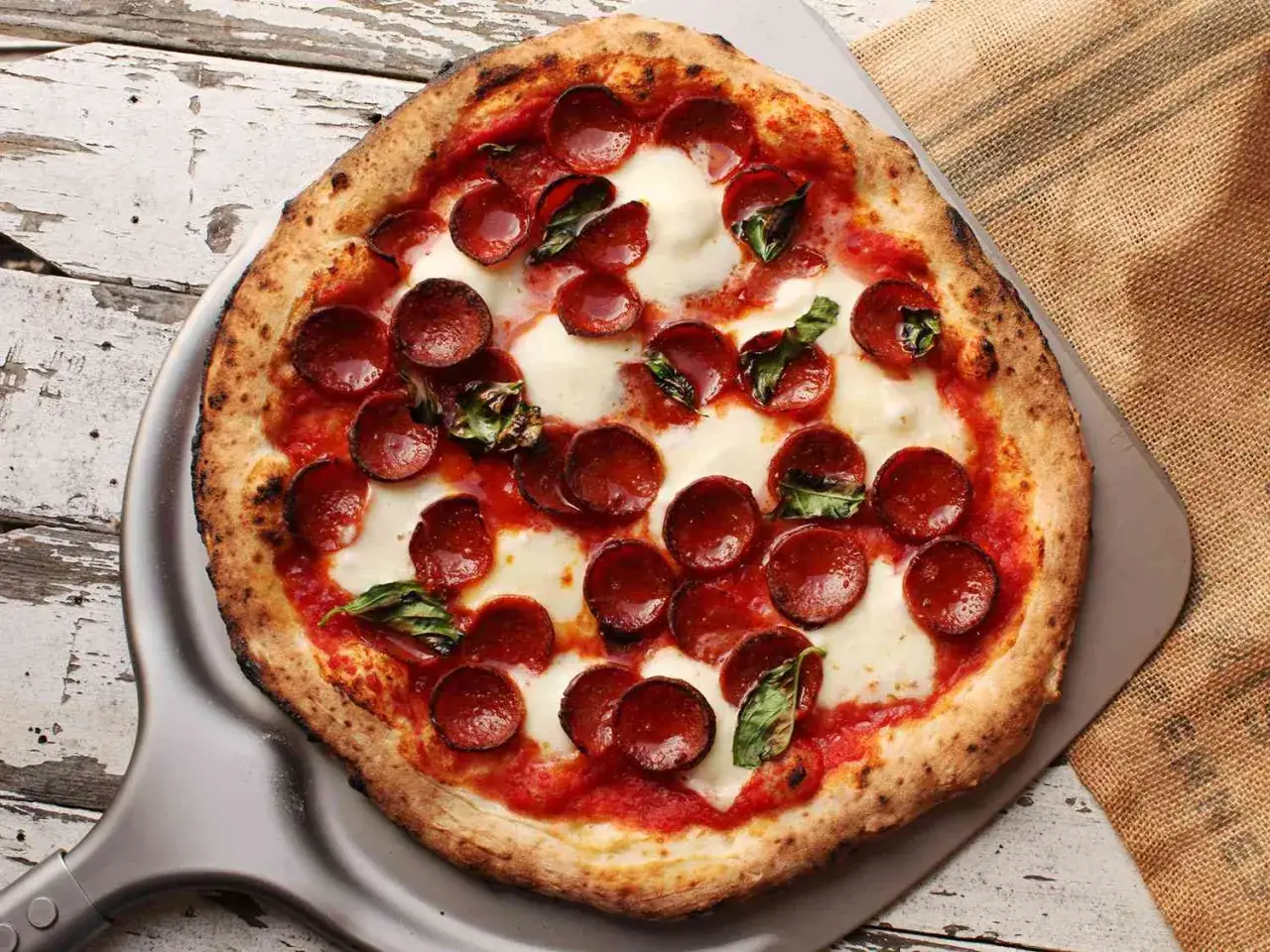Pizzaiolo z dumą prezentuje pizzę pepperoni z roztopionym serem i świeżą bazylią, prosto z pieca.