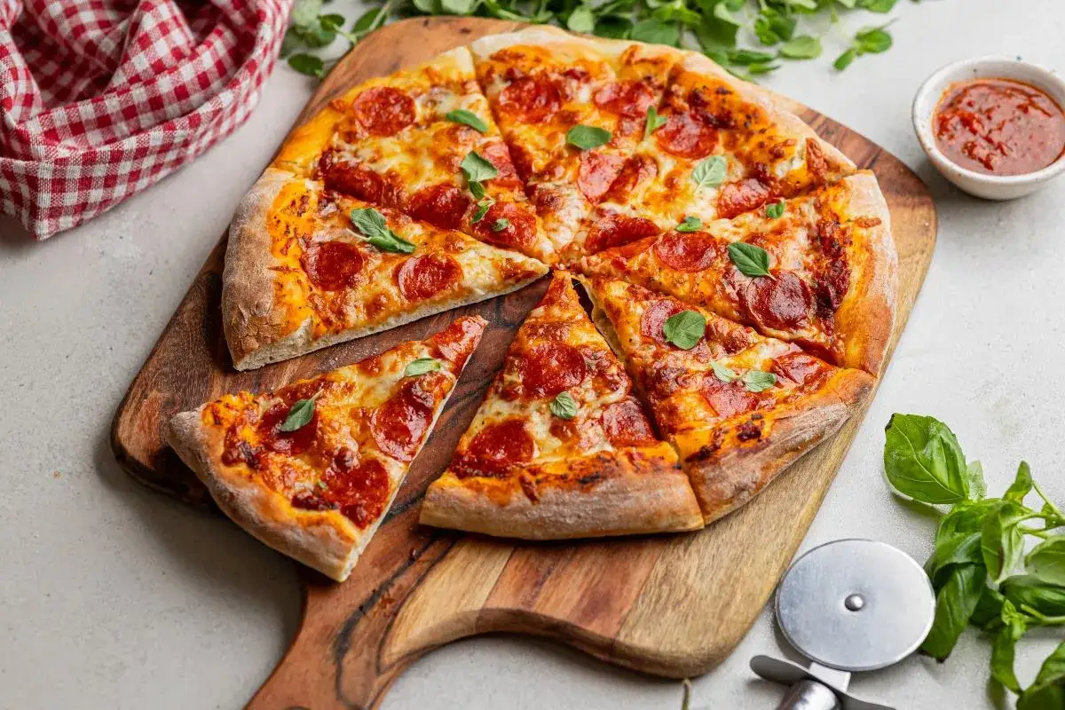 Apetyczna pizza pepperoni z ciągnącym się serem i świeżą bazylią, podana na drewnianej desce.